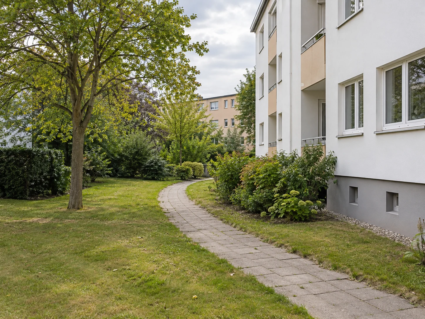 Fiktive Grünanlage mit Fußweg an einem Wohngebäude – KI-Illustration